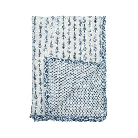 A folded indigo quilt with one side showing a geometric blue pattern and the other side displaying a floral print, placed on a neutral background.