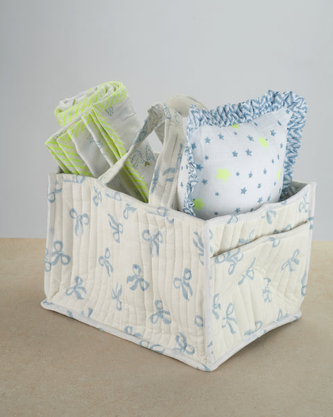 Quilted storage basket with baby items including blankets and a pillow on a neutral background