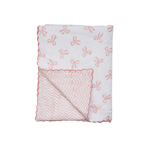 A reversible baby blanket with one side featuring a bow print and the other side a zigzag pattern, both in pink on a white background.